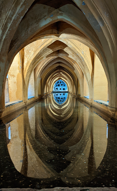 A set of arches reflected in a dark pool. At the end of the the pool is a large blue window of glass. all perfectly reflected in the still water